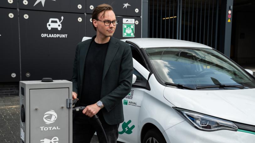 Man laadt elektrische auto buiten bij gebouw en parkeergarage