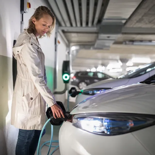 vrouw staat haar auto te laden in een overdekte parkeergarage